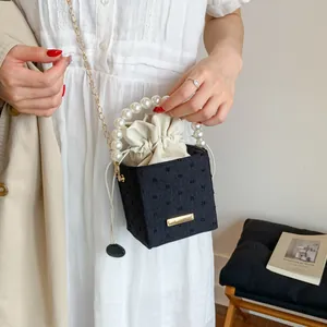 Detail of black bucket bag with pearl handle, gold chain strap, and drawstring insert