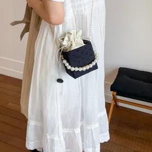 Detail of black bucket bag featuring large pearl handle and gold chain shoulder strap