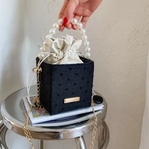 Detail of black cube bucket bag featuring large pearl handle and drawstring inner pouch