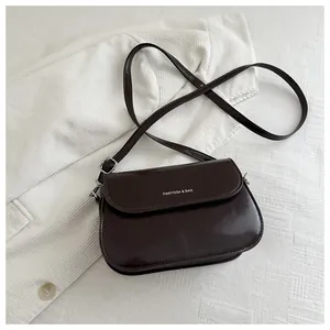 Detail van donkerbruine PU-lederen crossbodytas met witte belettering en zilveren gesp