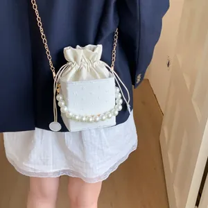 Detail view of white mini bucket bag with elegant pearl handle and gold chain strap