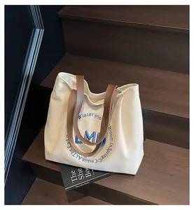 Detail of canvas tote bag featuring embroidered blue letters and brown leather handles