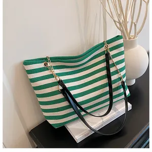 Detail view of green and white striped canvas tote bag with black leather handle and gold rings