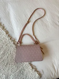 Détail d'un sac à main mauve texturé avec ferrures dorées et poignée supérieure nouée
