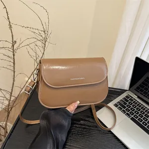 Bruine leren crossbodytas met logo op houten bureau in een sfeervolle setting