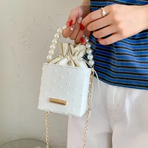Detail of white bucket bag with pearl handle, drawstring closure and polka dot texture