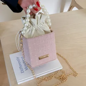 Detail of pink bucket bag featuring pearl handle, gold chain and drawstring closure