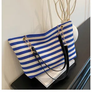 Detail of blue and white striped canvas tote bag with black strap and gold chain