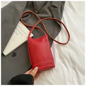 Detail of red lychee textured leather mini crossbody bag on a grey blazer background