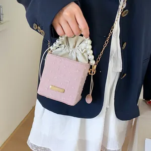 Detail of pink textured bucket bag with pearl handle and golden chain on a model