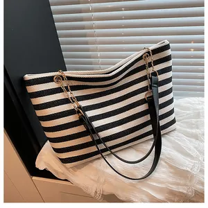Detail of striped tote bag with black and white patterns and gold chain leather handle