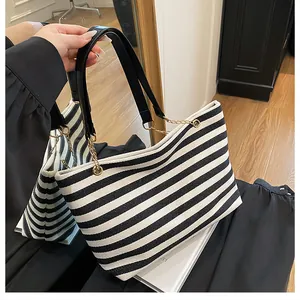 Close-up of black and white striped tote bag with wide leather strap and gold metal buckles