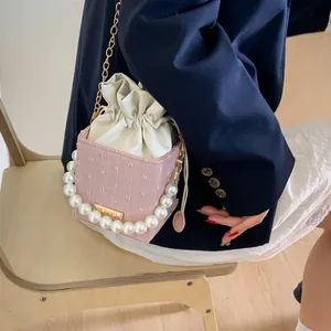 Pink bucket bag with pearl handle and metal chain shown on model in blue blazer