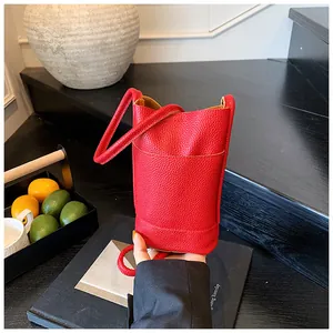 Detail of red lychee pattern leather bucket bag featuring a thin cylindrical shoulder strap