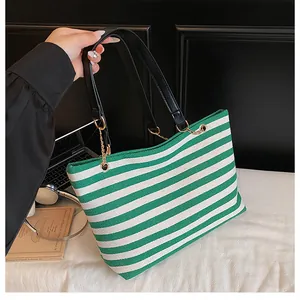 Detail of green striped canvas tote bag with black faux leather handles and gold chain