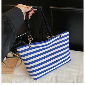 Detail of blue and white striped tote bag featuring black leather handles and gold chain links