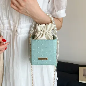 Light green bucket bag with pearl handle and chain strap shown in a lifestyle setting