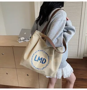 Detail of beige canvas tote bag featuring premium letter embroidery and brown strap