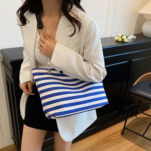 Blue and white striped tote bag with gold chain strap shown on a model in white blazer