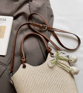 Detalle de bolso saco de paja con correa de cuero marrón y colgante de tulipán sobre blazer