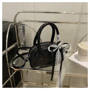 Detail of glossy black leather handbag with heart embossing and white lace bow decoration