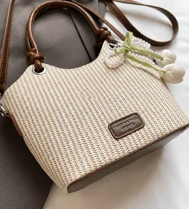 Detalle del bolso tipo cubo de paja tejida con asas de cuero y colgante de tulipán