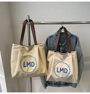 Detail of canvas tote bags in beige and off-white with blue embroidery and leather handles