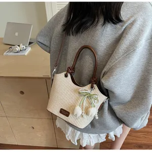 Detalle del bolso de paja tipo cubo con asas de cuero marrón y colgante de perlas
