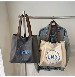 Detail of blue LMD letter embroidery on gray and white canvas tote bags with brown handles
