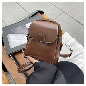 Detailed view of a brown faux leather mini crossbody bag with white contrast stitching and gold hardware
