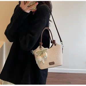 Detalle de bolso saco de paja con asa de cuero marrón y colgante de tulipán floral