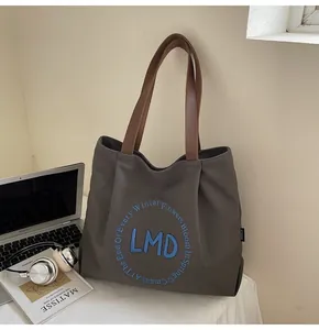 Detail of grey canvas tote bag with leather straps and blue circular embroidery on a desk