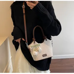 Detalle de bolso tipo cubo de paja con colgante de tulipán y etiqueta de cuero