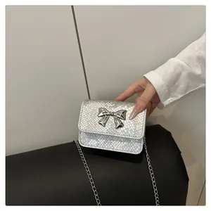 Detail of silver snake-patterned crossbody bag with a metallic bow and chain strap