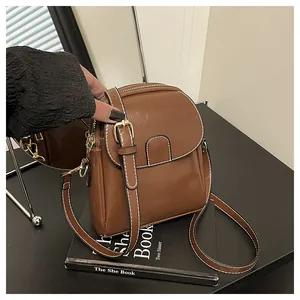 Close-up of brown crossbody bag featuring white contrast stitching and metallic buckle detail