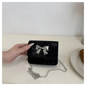 Close-up of black snake pattern leather crossbody bag with silver bow and chain
