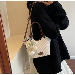 Detalle de bolso saco de paja con asa de cuero marrón y colgante de perla de tulipán