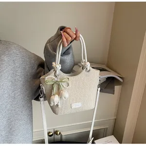 Detalle del bolso tipo cubo de paja con asa de cuero blanco y colgante de tulipán