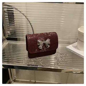 Close-up of wine red snake pattern mini bag with silver bow buckle on metallic stand