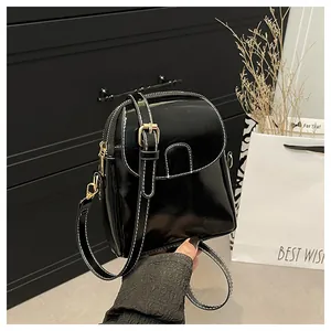 Close-up of black patent leather crossbody bag with white stitching and gold hardware