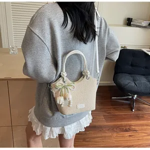 Detalle de bolso saco de paja tejida con dijes de perlas, lazo verde y correa de cuero