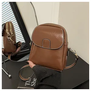 Detail view of small brown crossbody bag with dual zipper compartments and gold hardware