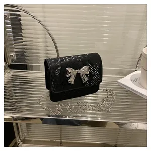 Close-up of black snake texture mini square bag with silver metal bow and chain strap