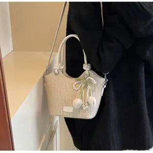 Detalle del bolso tipo cubo de paja con colgante de tulipa y asa de cuero anudada