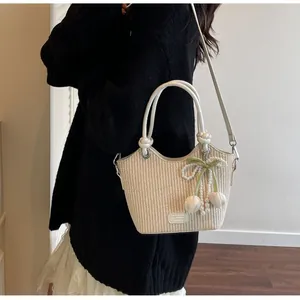 Detalle del bolso de paja tipo cubo con colgante de lazo de perlas y asas de cuero