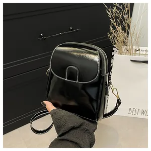 Close-up of a glossy black mini crossbody bag featuring white contrast stitching and hardware