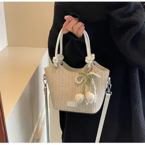 Detalle del bolso de paja tipo cubo con asas de cuero crema y colgantes de perlas