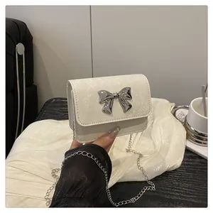 Detail of cream mini bag featuring a silver bow buckle and textured leather strap