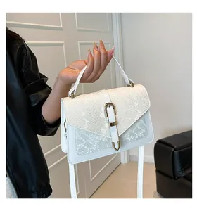 Detailed view of white snake-textured handbag with gold U-shaped buckle and top handle