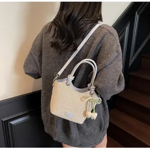 Detalle del bolso tipo cubo de paja con ribete de cuero gris y parche logo